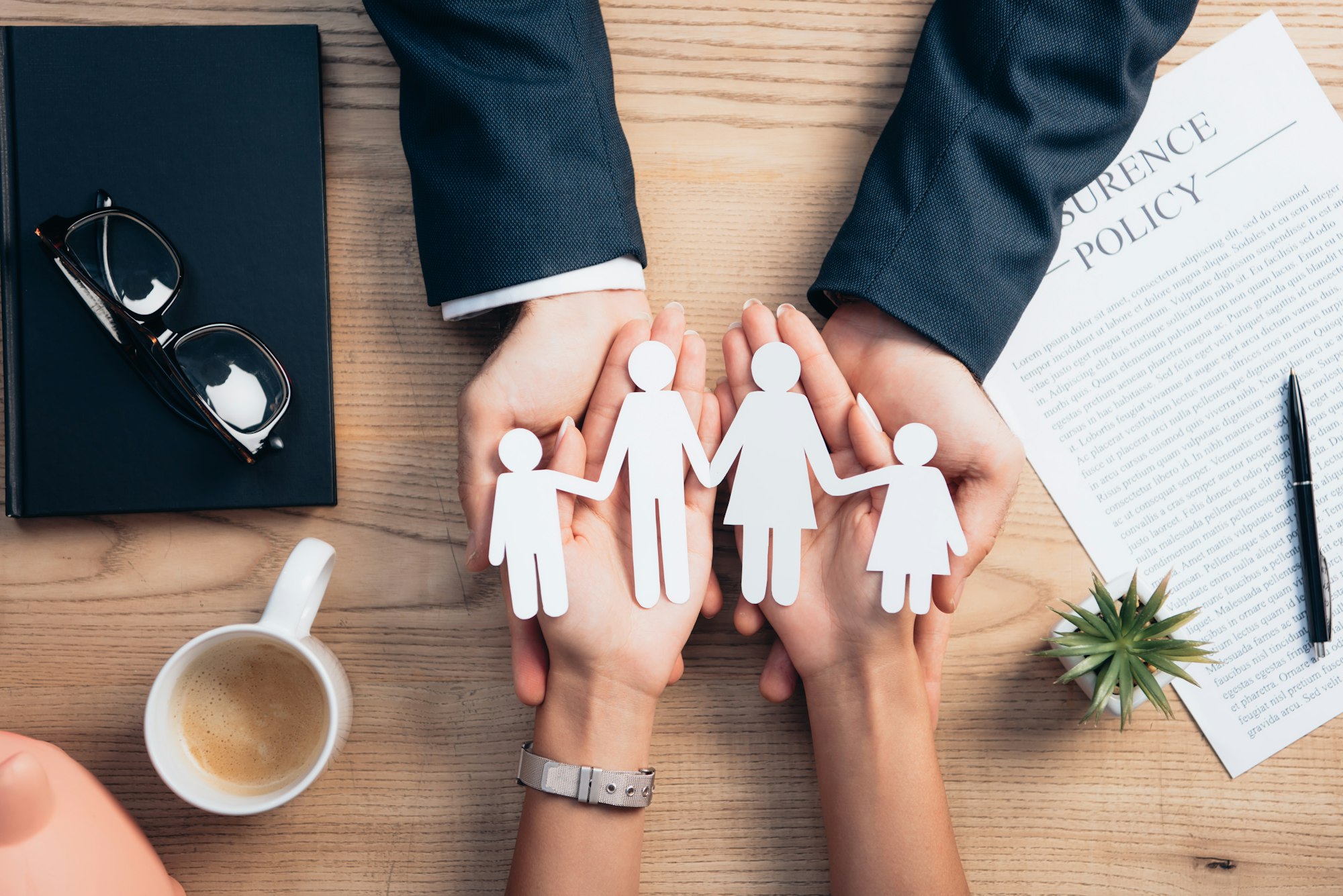 top view of lawyer and woman holding paper cut family near cup of coffee, insurance policy